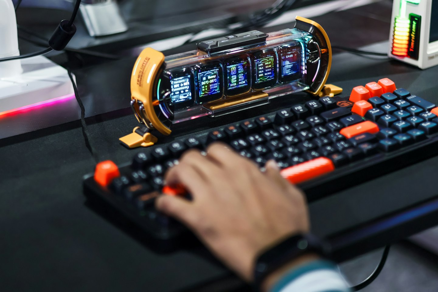 A hand types on a black keyboard with orange keys.